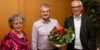 Drei fröhliche Menschen und Übergabe eines Blumenstraußes