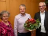 Drei fröhliche Menschen und Übergabe eines Blumenstraußes
