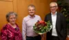 Drei fröhliche Menschen und Übergabe eines Blumenstraußes