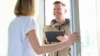 Mann mit Tablet steht vor Haustür, Frau öffnet die Tür