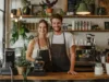 Zwei Baristas in einem Café stehen hinter dem Tresen und Lächeln den Betrachter an